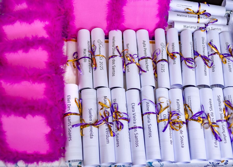 Canudos de formatura enfileirados, amarrados com fita roxa e dourada