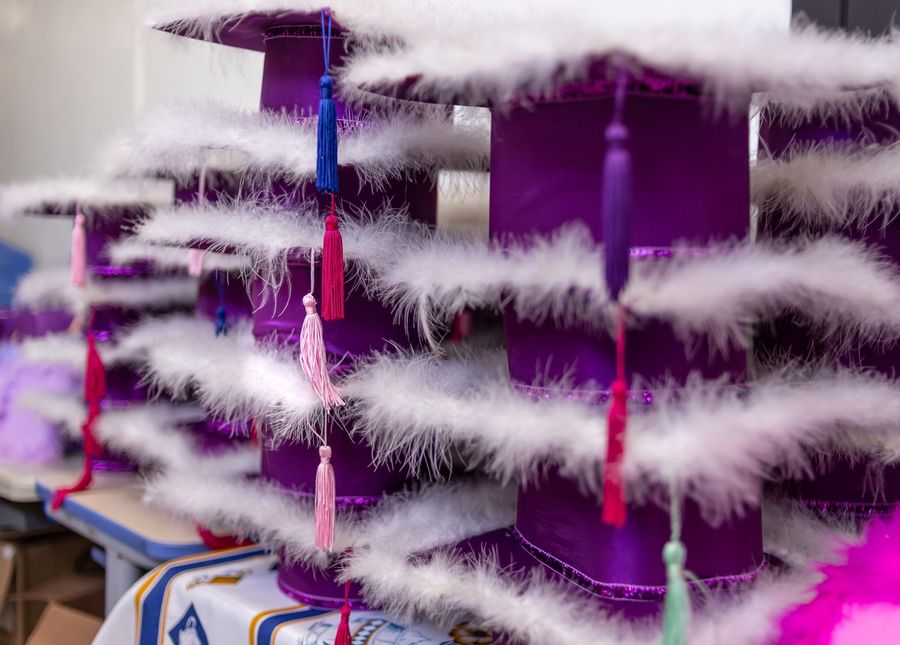 Capelos roxos com borlas coloridas e plumas brancas, prontos para a formatura