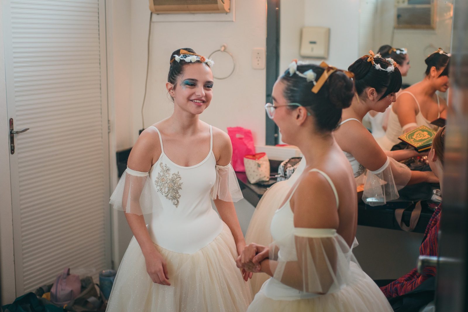 Duas bailarinas de tutu branco sorrindo de mãos dadas no camarim antes do espetáculo