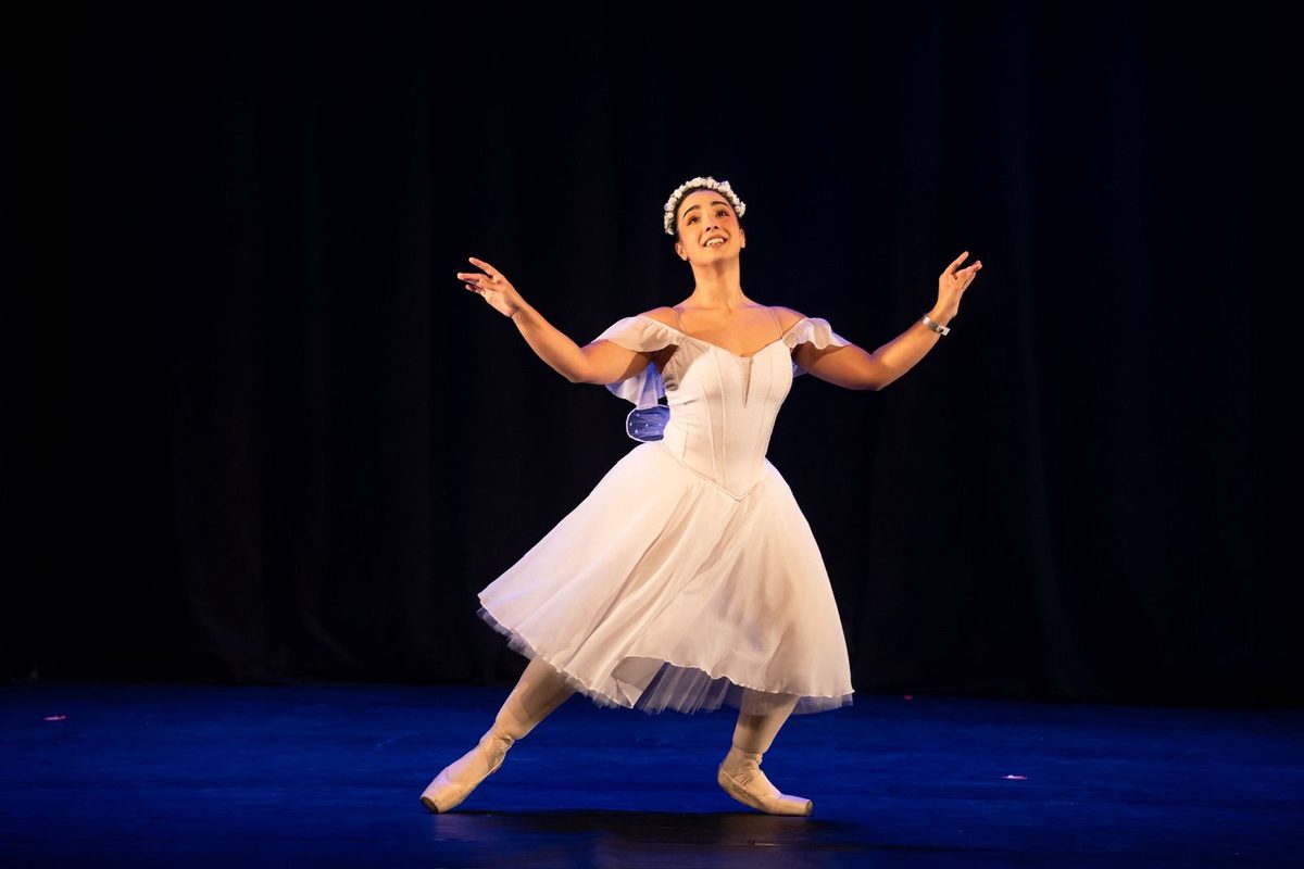 Eduarda Soares da Silveira no palco, de tutu branco e coroa de flores, com os braços abertos