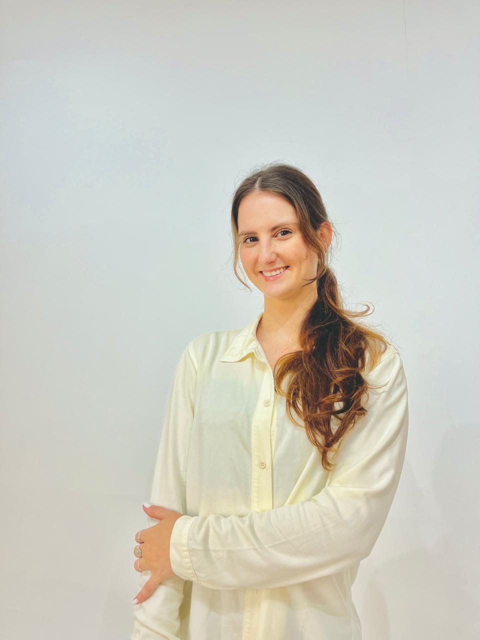 Giovana Isotton, de camisa branca, sorrindo com os braços cruzados